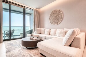 A modern living room with a beige sectional sofa, a round coffee table, and a large window offering a view of the city.