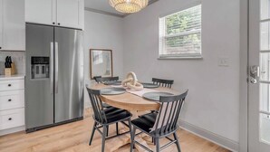 Une cuisine moderne avec un réfrigérateur en acier inoxydable, une table de salle à manger ronde en bois et des chaises noires, ainsi qu’un luminaire suspendu.