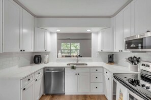 Une cuisine moderne avec des meubles blancs, un lave-vaisselle en acier inoxydable, un four à micro-ondes et un four traditionnel.