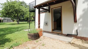 A house with a covered porch, a wooden door, and a small garden area with a wooden planter and gravel path. - Hillcroft (Kenilworth)