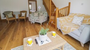 A cozy living room with a wooden staircase, a sofa, a chair, and a small table with a plant and two cups. - Hillcroft (Kenilworth)