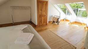 A bedroom with a large bed, a wooden door, a radiator, a window, and a skylight. - Hillcroft (Kenilworth)