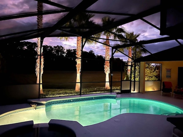 An outdoor swimming pool with a covered area, palm trees, and a view of the sky.