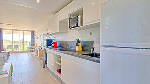 Eine moderne Küche mit weißen Schränken, einer schwarzen Arbeitsplatte und einem Edelstahlspülbecken. Durch ein großes Fenster ist ein Essbereich mit Tisch und Stühlen zu sehen.