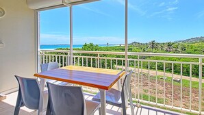 Ein Balkon mit Tisch und Stühlen, der auf eine Küstenlandschaft mit viel Grün und blauem Himmel blickt.