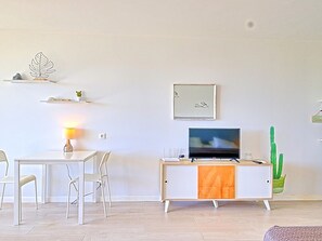 A modern living room with a white sofa, a dining table with chairs, a flat-screen TV on a wooden cabinet, a cactus plant, and wall art. - Spacious Studio in Saint Martin with Terrace and Equipped Kitchen (Saint-Martin)