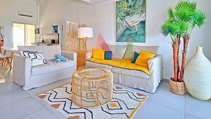 A modern living room with a sofa set, a round wicker coffee table, and a large painting of a tropical scene.