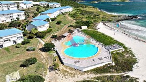 A resort with multiple white buildings, a central swimming pool, and a beach.