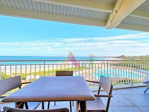 A balcony with a view of the ocean, a pool, and a beach.
