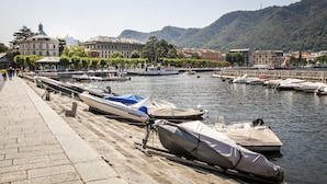 A waterfront with boats docked along the pier, a clear sky, and buildings in the background. - Lakeside (Como)