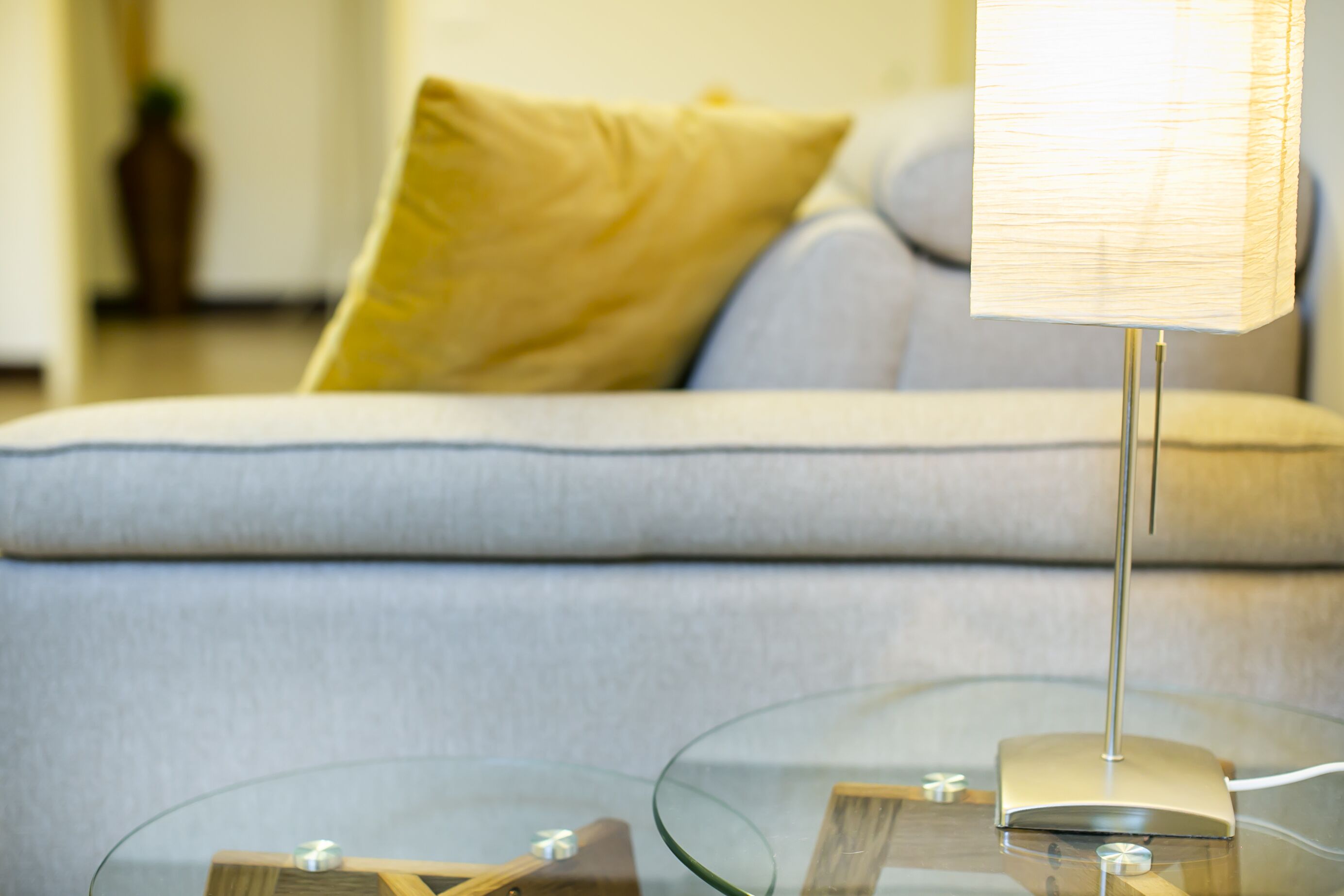 Un salon moderne avec une table basse en verre, une lampe et un canapé agrémenté de coussins.