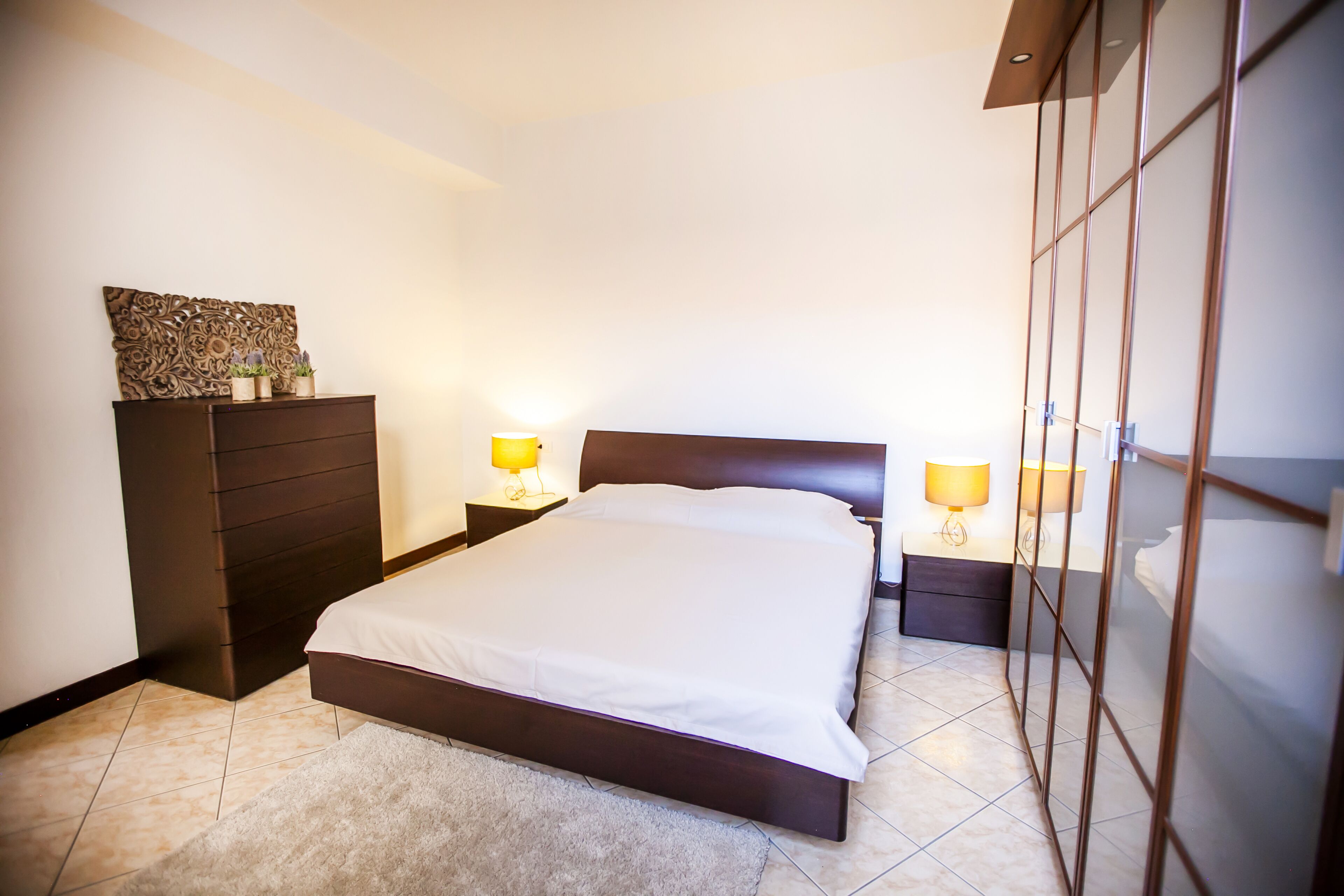 A neatly arranged bedroom with a bed, dresser, nightstands, and wall decor.