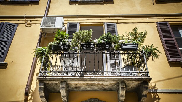 A yellow building with a balcony featuring wrought iron railings and potted plants. - Lakeside (Como)