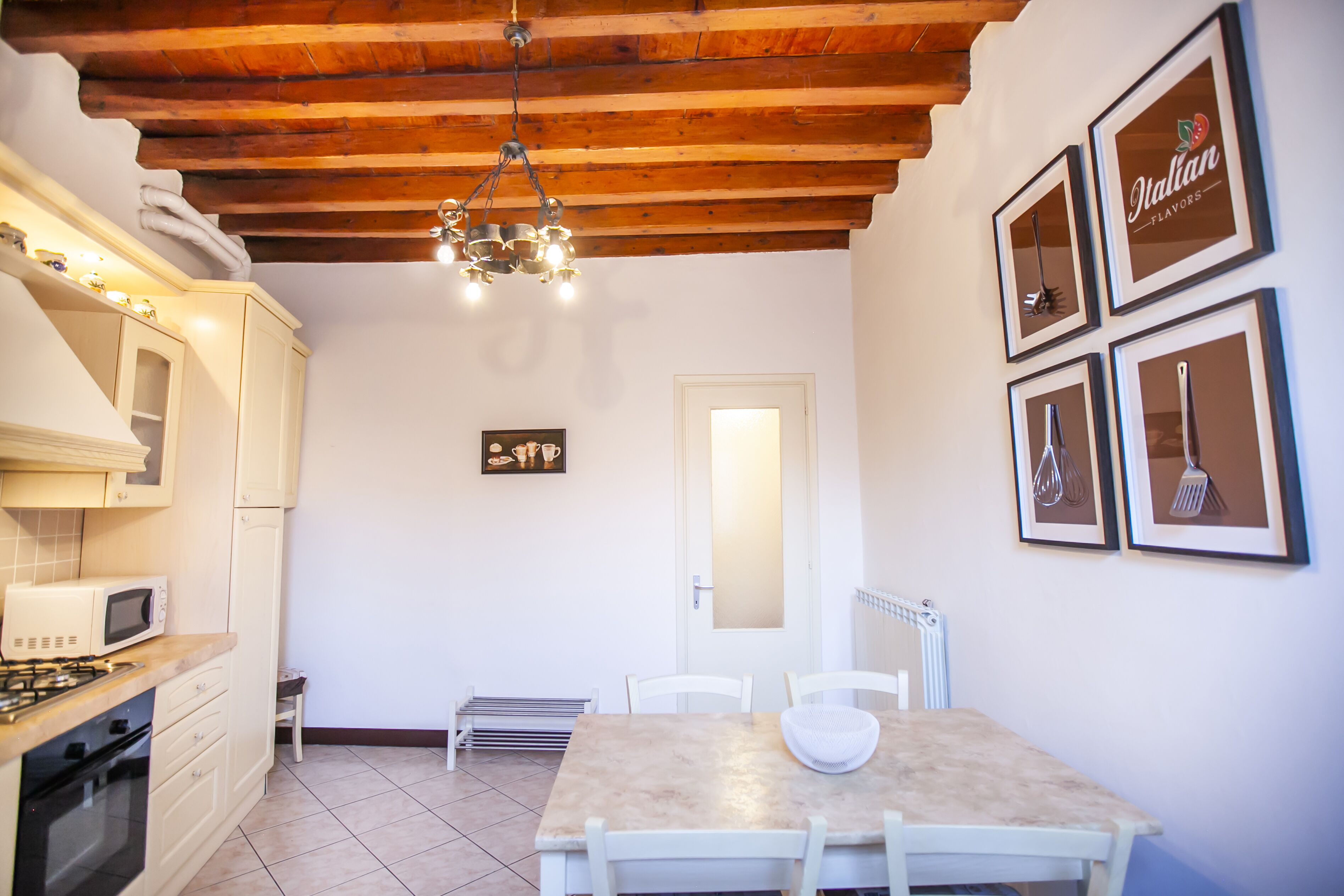 A kitchen with wooden beams, a dining table, chairs, a microwave, and framed pictures on the wall.