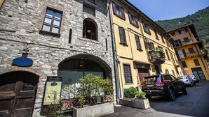A stone building with a wooden entrance, a signboard, and a parked car. - Lakeside (Como)