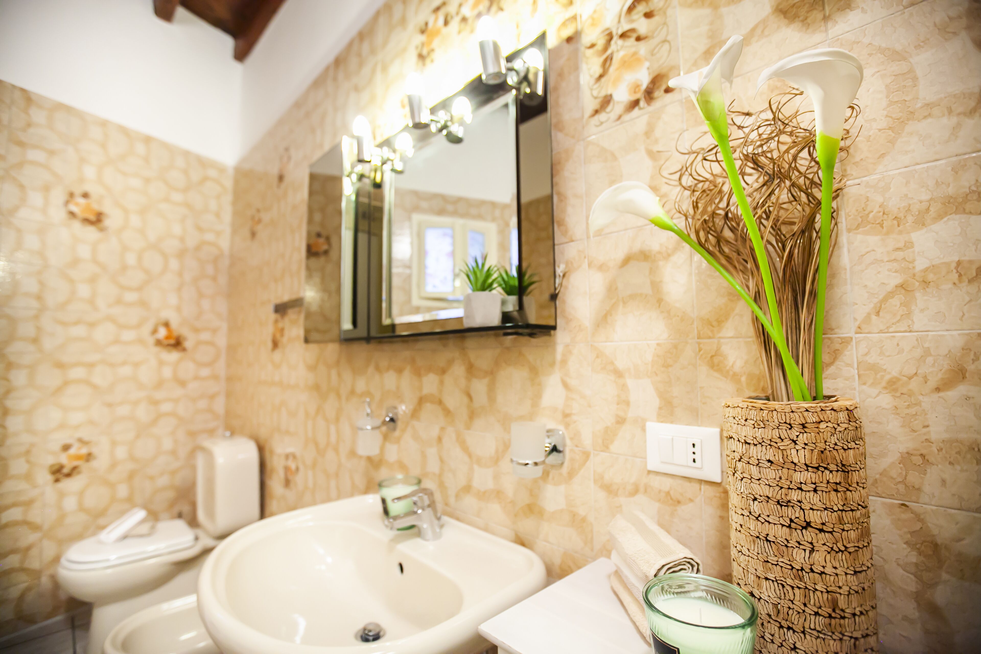 A bathroom with a sink, mirror, and a decorative vase with green stems.