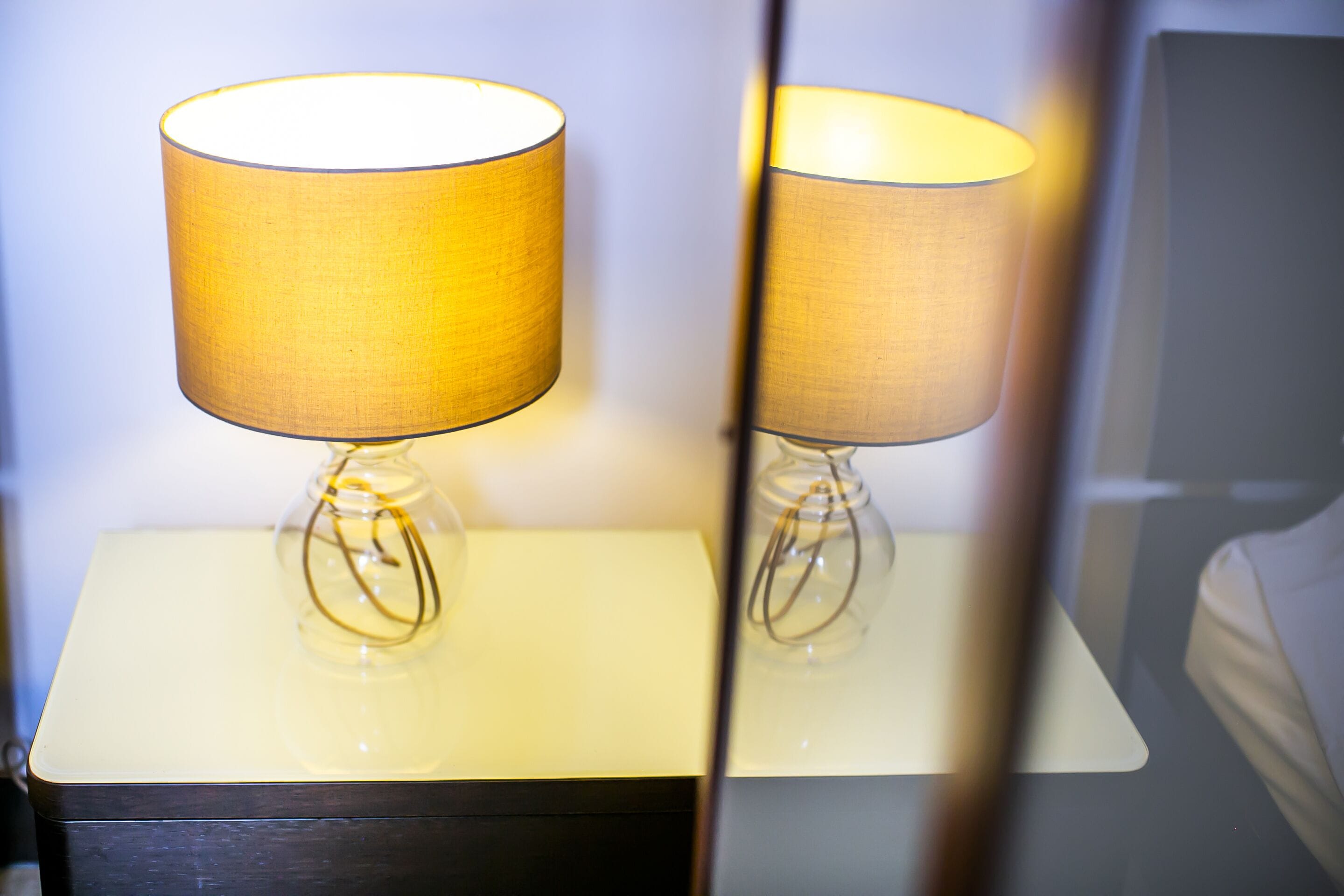 Um abajur sobre uma mesa de cabeceira, com um espelho refletindo a luz.