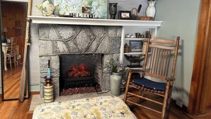 A cozy living room with a stone fireplace, a wooden chair, and a bookshelf.