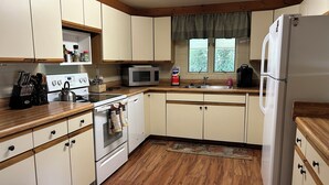 A kitchen with wooden cabinets, a stove, a microwave, a refrigerator, and a window with curtains.