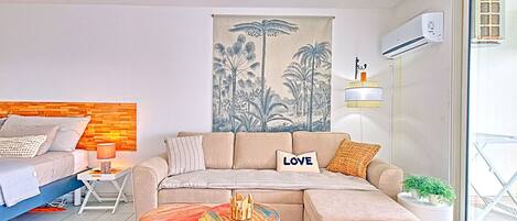 A modern living room with a sectional sofa, a small wooden table, and a painting of tropical scenery.