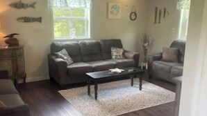 A living room with a dark wood floor, a grey sofa, a coffee table, and a ceiling fan.