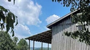 A rustic wooden building with a balcony, surrounded by greenery and a clear sky.