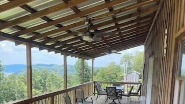 A wooden deck with a table and chairs, overlooking a forested landscape.