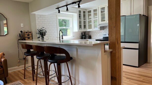 Una cocina moderna con armarios blancos, una isla central con taburetes de bar, un refrigerador de acero inoxidable y una ventana que proporciona luz natural.