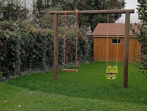 A wooden swing set in a grassy yard with a wooden shed in the background. - Spacious 5-Bedroom Cottage Near Paris with Garden and Parking (Nargis)