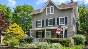 A two-story house with a front porch, a flag, and a well-maintained garden. - Historic Home Central Flourtown Hosted By StayRafa (Flourtown)