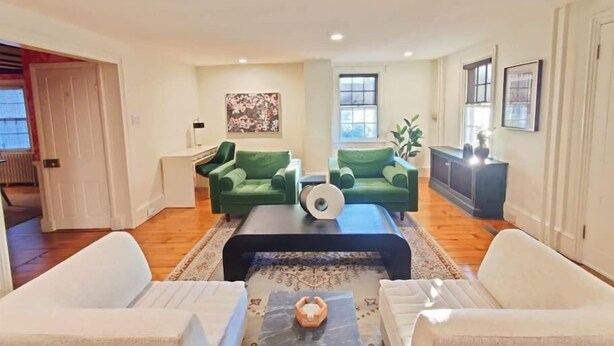 A spacious living room with a large window, a green sofa set, a coffee table, and a white armchair. - Historic Home Central Flourtown Hosted By StayRafa (Flourtown)