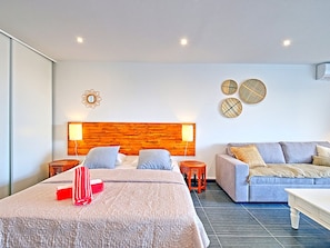 A modern hotel room with a large bed, a sofa, two nightstands, and a wooden headboard.