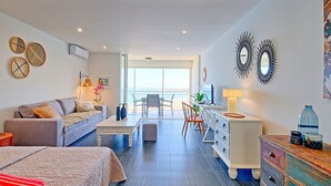 A modern hotel room with a balcony, a sofa, a desk, and a dresser.