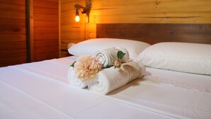Una cama bien hecha con sábanas blancas y una toalla enrollada con una flor.