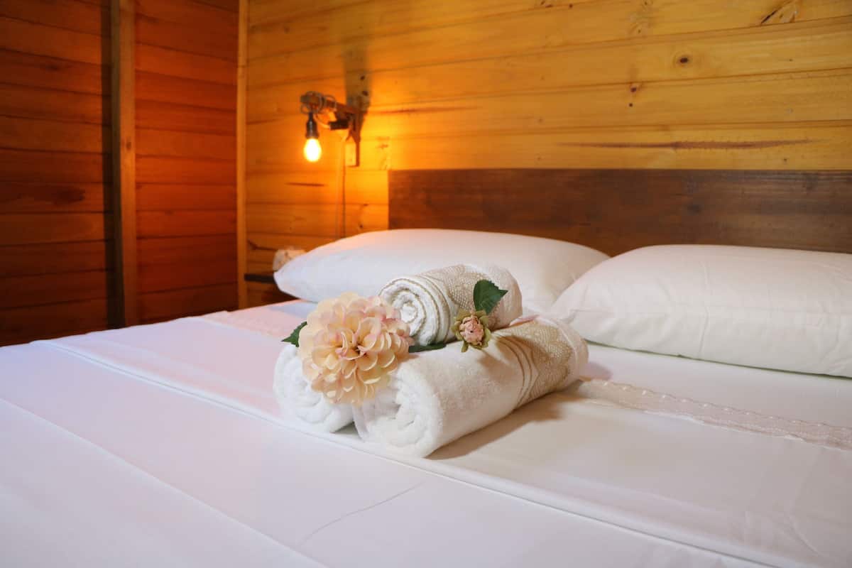 A neatly made bed with white linens and a rolled towel with a flower.