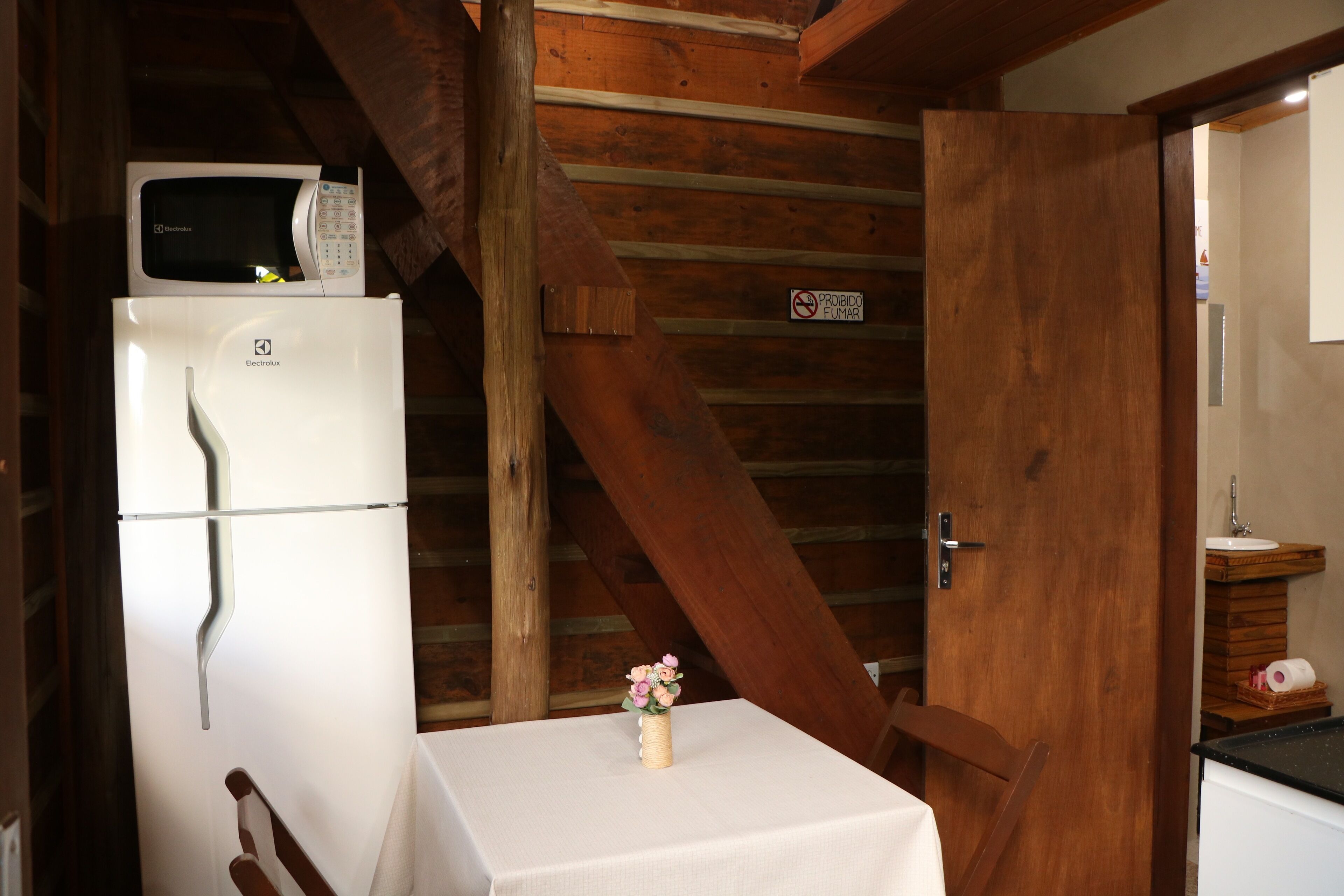 A kitchen with a white refrigerator, a microwave on top, a wooden ceiling, and a table with a vase of flowers.