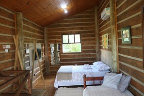 A log cabin room with two beds, a wooden ceiling, and a window.