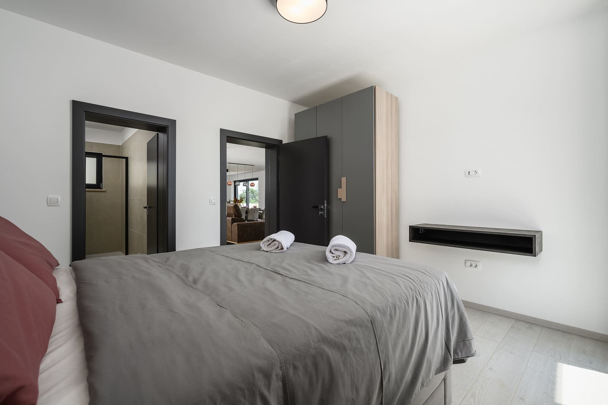 A modern hotel room with a large bed, a wardrobe, a built-in shelf, and a mirror.