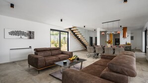 A spacious living area with a brown leather sofa, a coffee table, and a dining area with a staircase. - Villa de la Vie with Heated Swimming Pool (Sveti Bartul)