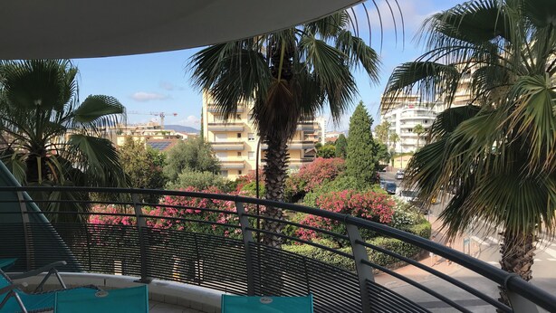 A balcony with turquoise chairs, a railing, and a view of buildings and greenery. - Appt Standing Face à la Mer (Fréjus)