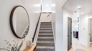 A modern interior with a staircase, wooden console, mirror, and a hallway leading to a kitchen area.