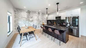 A modern kitchen with a central island, stainless steel appliances, and a dining area with a wooden table and chairs.