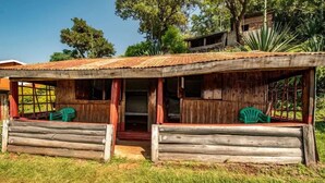 A rustic wooden structure with a corrugated metal roof, a porch with wooden railings, and two green plastic chairs.