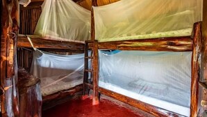 A rustic wooden cabin with two bunk beds, each covered with mosquito netting.