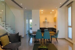 Uma sala moderna com um sofá, uma mesa de jantar com cadeiras, uma escada e uma área de cozinha.