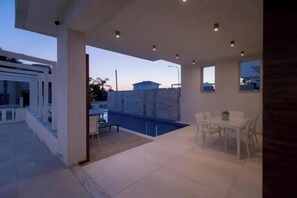 Un patio exterior moderno con piscina, zona de comedor y vistas del vecindario.