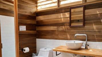 Un baño con paredes de madera, un inodoro blanco, un lavabo con espejo y una ventana sobre el lavabo.