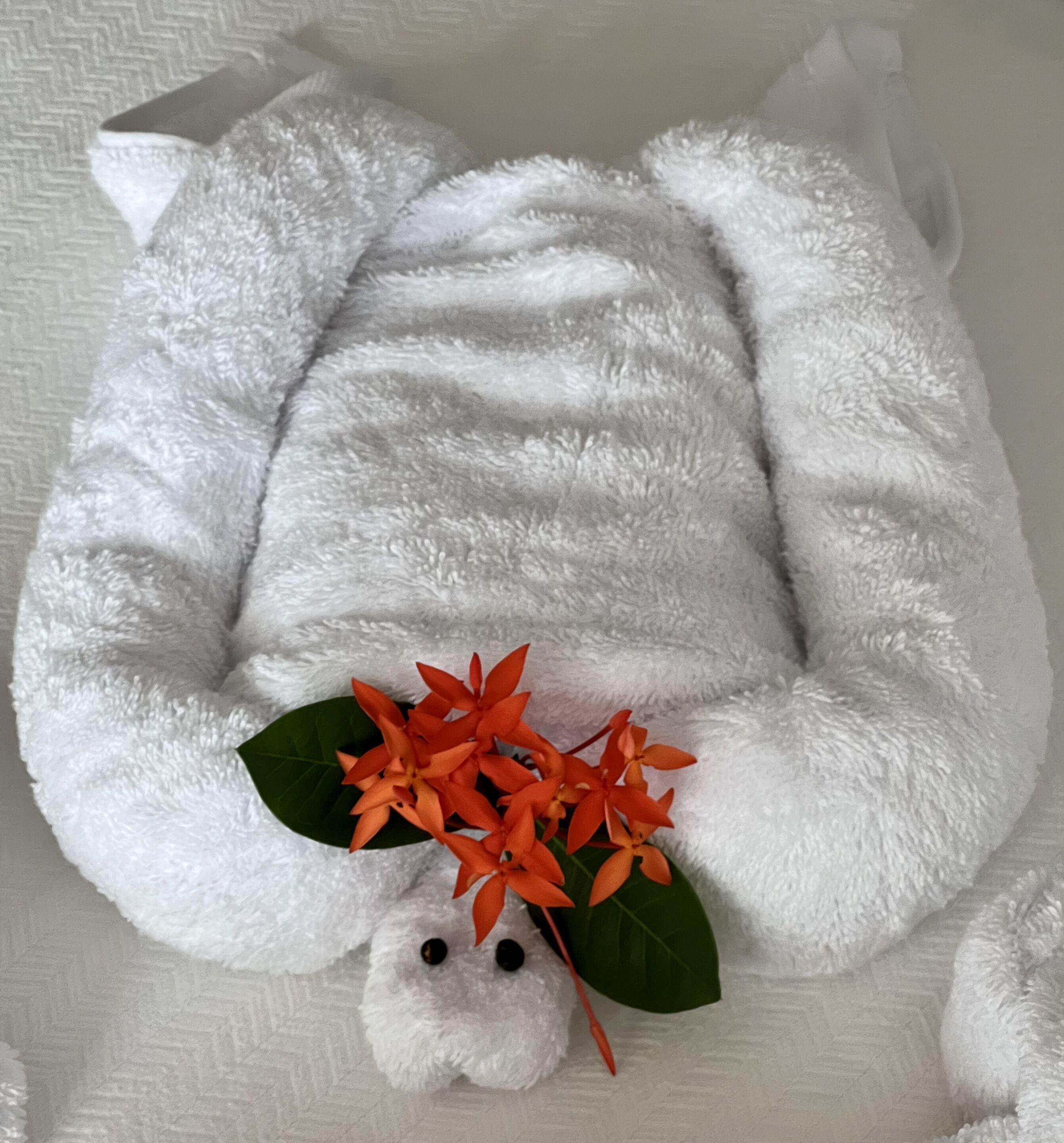 Ein weißer, flauschiger Sitzsack mit einer kleinen, weichen Tierfigur und orangefarbenen Blüten.