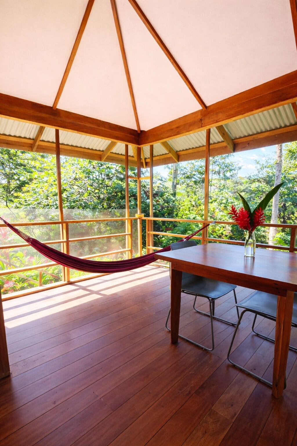 Una terraza de madera con una hamaca, una mesa y sillas, con vistas a un jardín exuberante.
