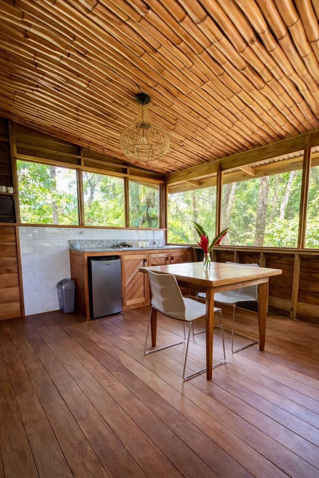 A wooden interior with a kitchen area, a dining table, and large windows.